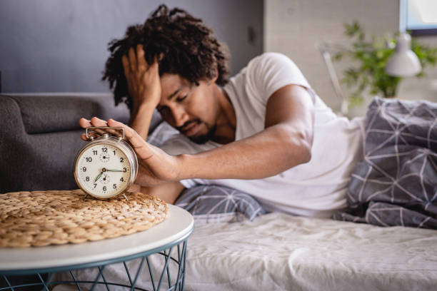 Homme désactivant son réveil alors qu'il est encore fatigué après une mauvaise nuit à cause de l'insomnie