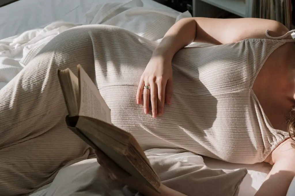 Femme enceinte allongée sur un sofa et lisant un livre